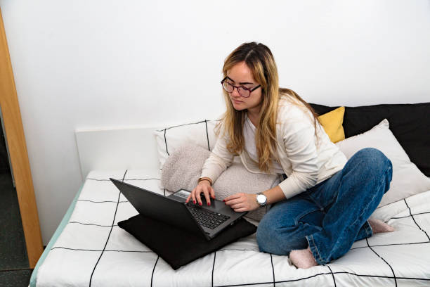 istock Young woman working on laptop sitting on her bed 1175558576