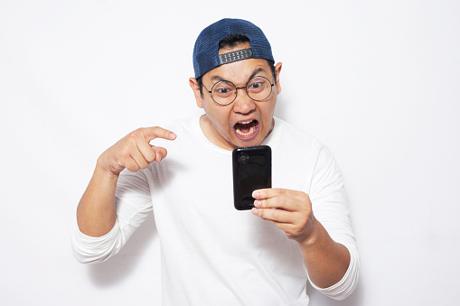 Attractive young Asian man reading texting chatting on his phone, mad angry expression