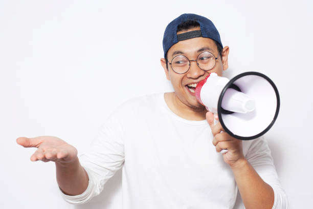 Young Asian man wearing casual white shirt using megaphone, shouting and smiling. Close up body portrait. Marketing promotion concept
