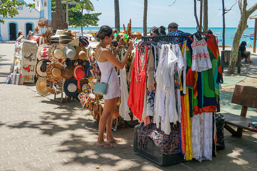 Tourist looking at clothes at a little stand  in the famous main walking street for tourists and shopping in Praia Do Forte, State of Bahia, Brazil