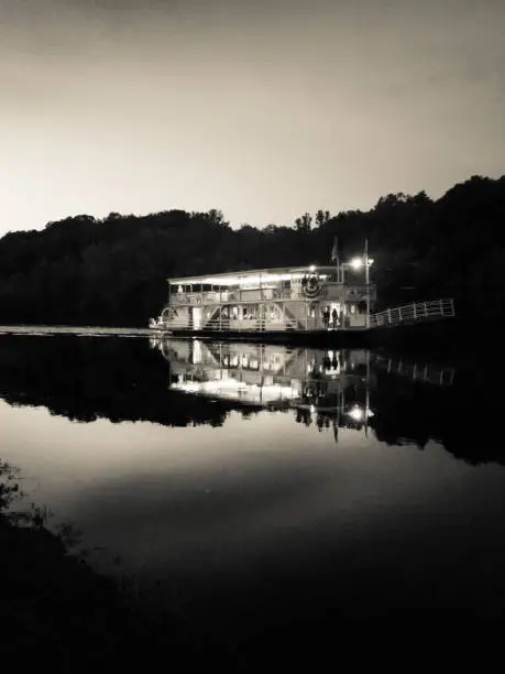 An older paddle wheel boat going up the river at sunset done in black and white