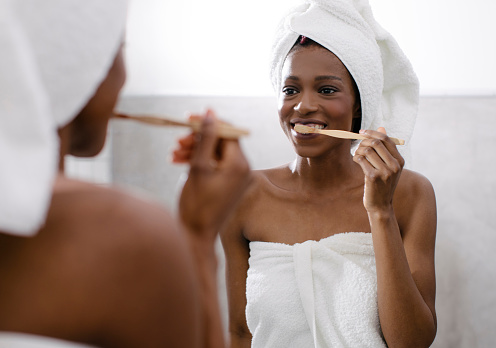Beautiful smiling African woman brushing her teeth at the bathroom.