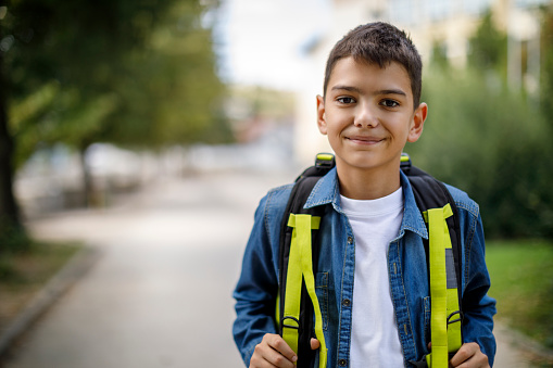 Niño adolescente sonriente con bolsa de la escuela en frente de la escuela photo