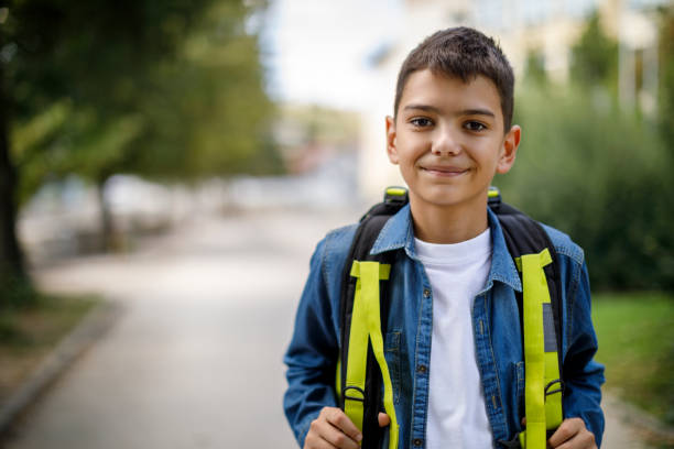 adolescente sorridente con borsa da scuola di fronte a scuola - bambini maschi immagine foto e immagini stock
