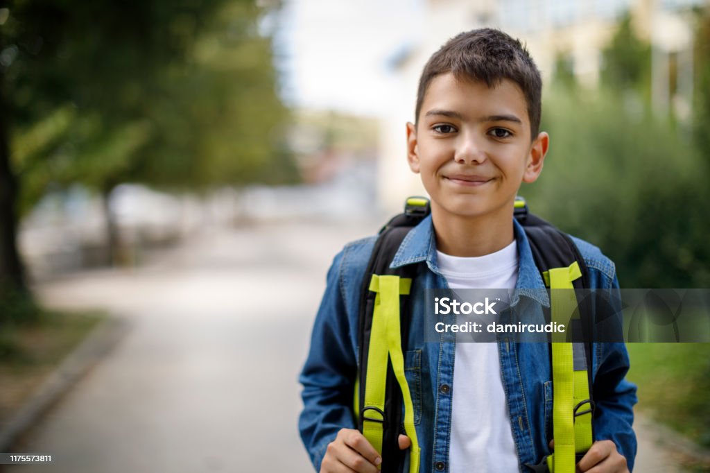 Smiling teenage boy with school bag in front of school Child Stock Photo