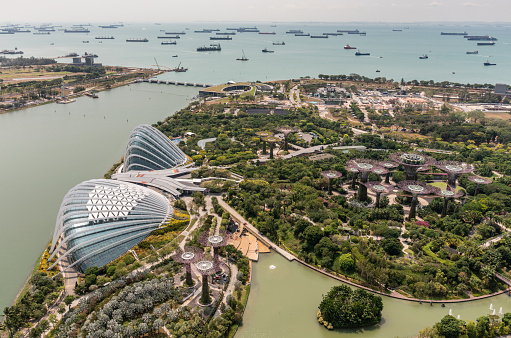 Singapore - March 21, 2019: Birds eye view on green Gardens by the Bay and its two super domes with tens of ships waiting in Singapore Strait.