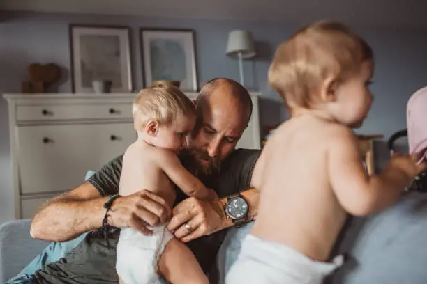 Cheerful Father With twins daughters On Sofa At Home. They fooling around and enjoy in life