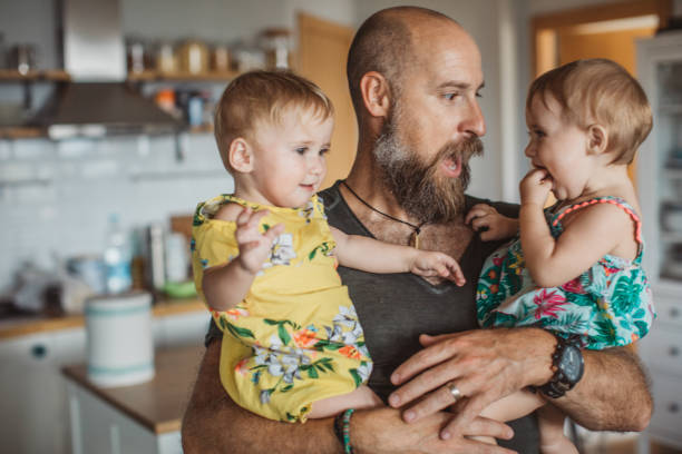 Spending time with father Cheerful Father with twins daughters in kitchen At Home. They are one happy family twin stock pictures, royalty-free photos & images