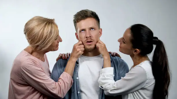 Mother and wife admiring mature man and pinching cheeks, overprotection concept