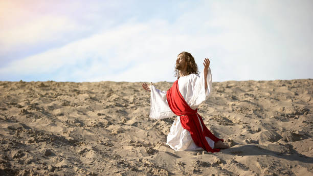 istock Righteous man kneeling in desert, praying to god with raised hands, confession 1175583436