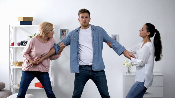 In-law conflict, mother and wife pulling young man in different directions In-law conflict, mother and wife pulling young man in different directions mother in law stock pictures, royalty-free photos & images