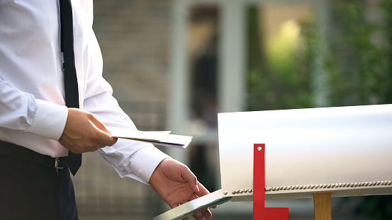 Businessman sending letters and bills, putting them into mailbox near house