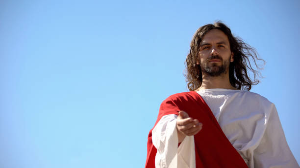 istock Jesus in white robe stretching hand against blue background, asking Lord help 1175583527
