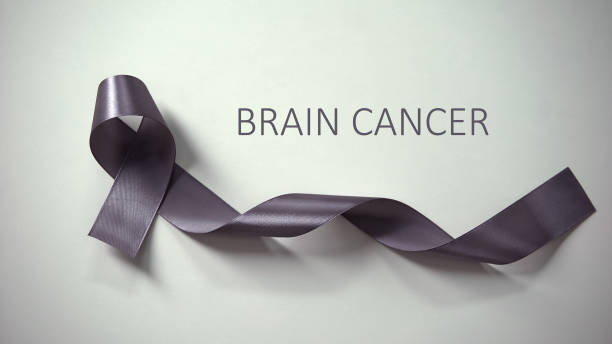 istock Brain cancer inscription, gray ribbon lying on table, awareness campaign, ad 1175583681