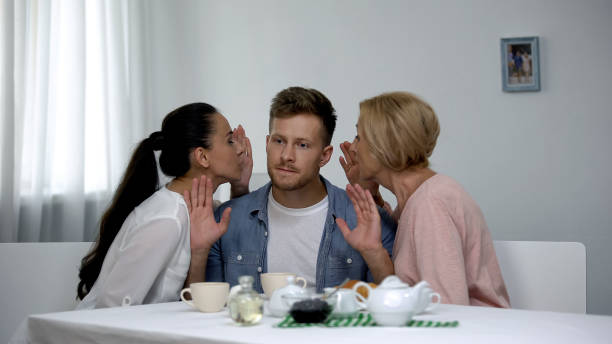 Irritated man listening wife and mother-in-law whispering on ear, problems Irritated man listening wife and mother-in-law whispering on ear, problems annoying mother in law stock pictures, royalty-free photos & images