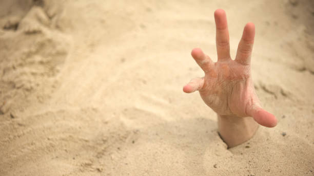 Hand sinking in quicksand, trying to get out, tips to survive in desert, buried stock photo