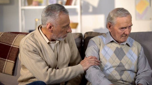 istock Old man supporting upset friend sitting sofa home, health problems, life crisis 1175584518