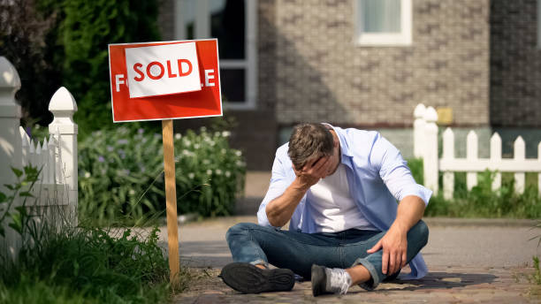 istock Extremely depressed man sitting on ground by sold signboard, financial problems 1175584699
