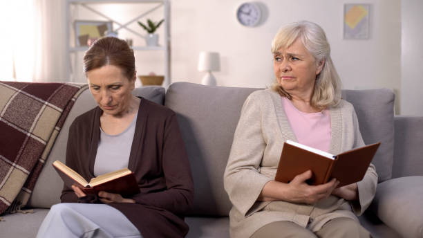 istock Angry aged lady looking senior woman reading book sofa, communication conflict 1175584883