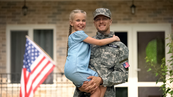 Guapo soldado de EE.UU. con uniforme militar sosteniendo feliz hija, regreso a casa photo