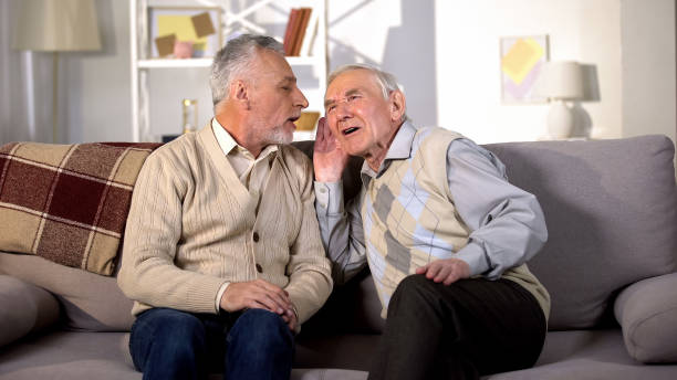 istock Old man talking to deaf friend sitting on sofa at home, hearing disease, problem 1175585209