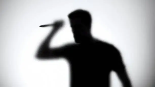 Photo of Silhouette of a man with knife standing behind glass wall, thriller