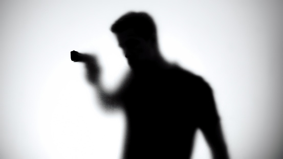 Shadow of male aiming gun through glass wall