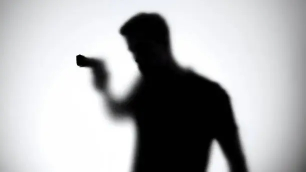 Shadow of male aiming gun through glass wall