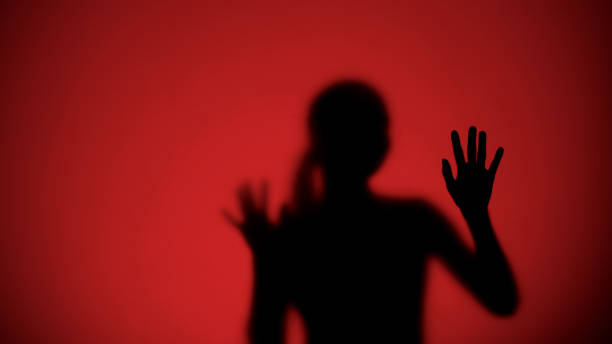 istock Female silhouette behind glass escaping from danger, red lights on background 1175587692
