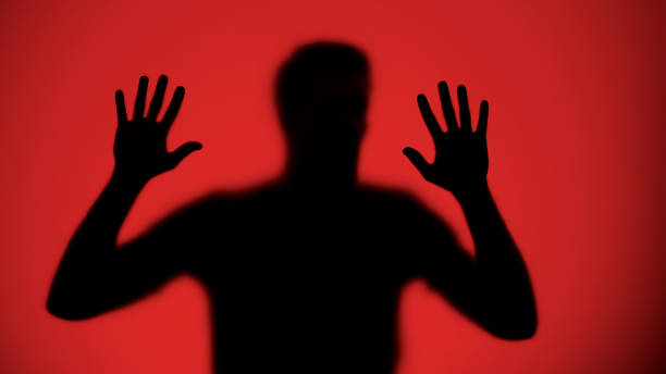 istock Male silhouette touching glass wall, red lights background, kidnapping victim 1175587722