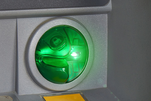 Round green ATM slot for debit and credit cards close-up. Green backlight. Safe back-office transactions, money transfers, cash withdrawals, payment for services and goods online.