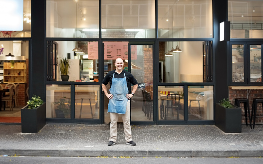 Portrait of confident male barista standing with his hands on hips outside the restaurant