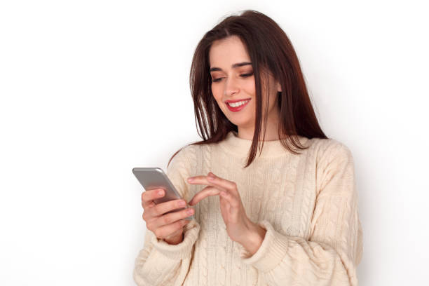 istock Young woman studio standing isolated on white browsing smartphone cheerful 1175599930