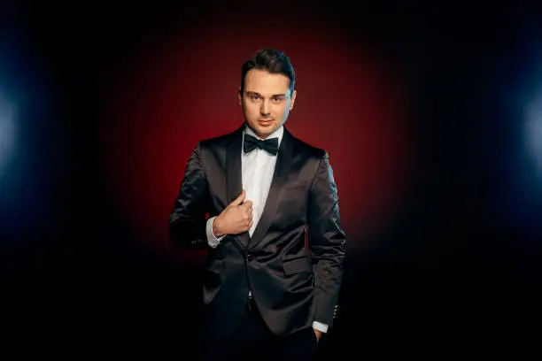 Professional showman wearing suit standing isolated on black and red background posing to camera smiling playful