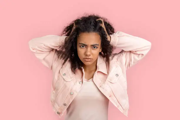 Photo of Freestyle. African girl in denim jacket standing isolated on pink messing hair looking camera angry close-up