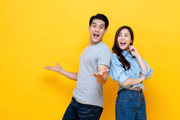 Attractive happy amazed young Asian couple Attractive smiling young Asian couple being happy and amazed isolated on yellow studio background male meaning stock pictures, royalty-free photos & images