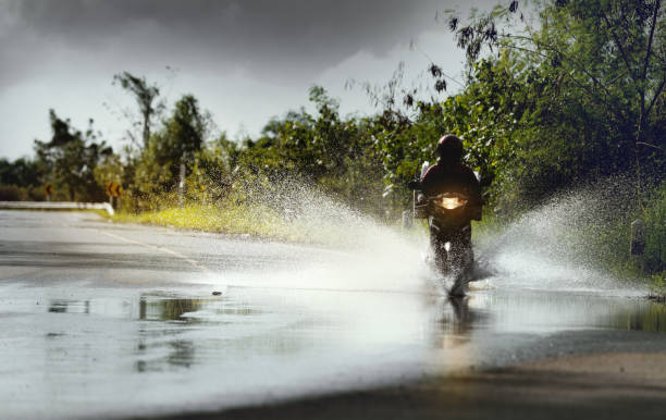 motocicleta correr a través del agua de inundación después de la lluvia dura con el agua pulverizada de las ruedas, detener la acción. - rain tornado overcast storm fotografías e imágenes de stock