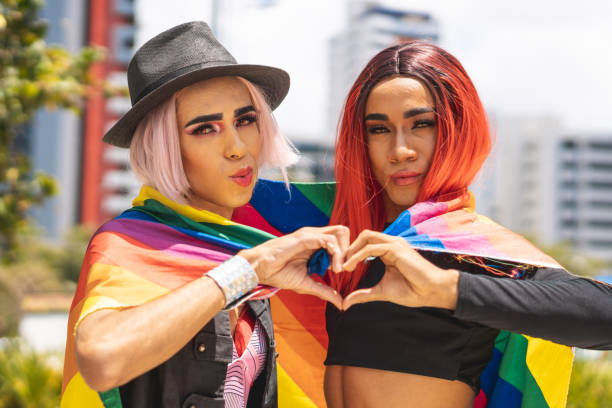 shemales enveloppés dans le drapeau d'arc-en-ciel et affichant la forme de coeur avec des mains - travesti photos et images de collection