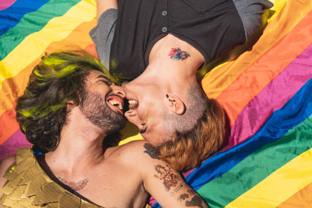 homosexual couple sunbathing lying on the rainbow flag - flag rainbow gay pride flag gay man imagens e fotografias de stock