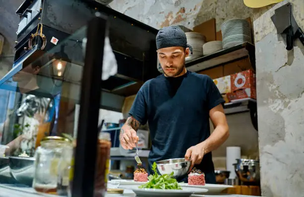 Shot of a young man preparing a steak tartare dish in a commercial kitchen