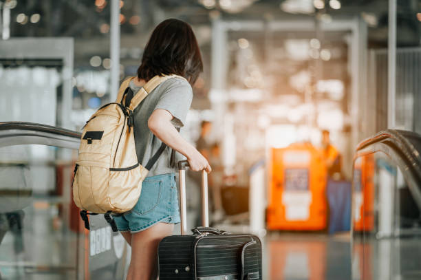 istock Young woman pulling suitcase in modern airport terminal. Travelling guy with his luggage while waiting for transport. Rear view. Copy space 1175626504