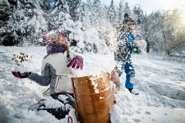 Kids hiding behind a toboggan, having a snowball fight. Brother and sister are enjoying beautiful winter day.\nNikon D850