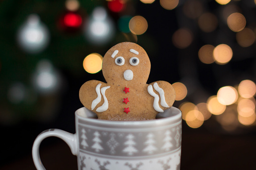 gingerbread man cookie in a cup with hot drink with christmas lights on a background