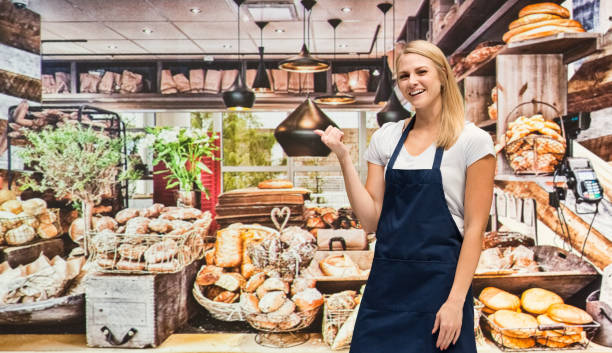 one person / waist up of blond hair caucasian female / young women caterer / baker / retail occupation cooking / preparing food / standing at the bakery / restaurant in the store wearing apron / uniform / t-shirt / shirt and celebration / retail - thank you excitement waist up horizontal imagens e fotografias de stock