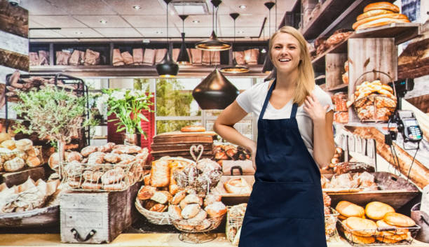 one person / waist up of blond hair caucasian female / young women caterer / baker / retail occupation cooking / preparing food / standing at the bakery / restaurant in the store wearing apron / uniform / t-shirt / shirt and celebration / retail - thank you excitement waist up horizontal imagens e fotografias de stock