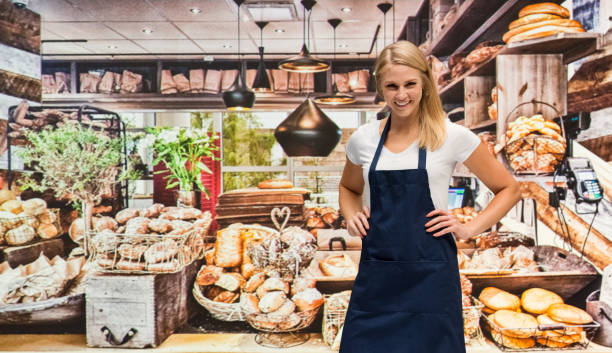 one person / waist up of blond hair caucasian female / young women caterer / baker / retail occupation cooking / preparing food / standing at the bakery / restaurant in the store wearing apron / uniform / t-shirt / shirt and celebration / retail - thank you excitement waist up horizontal imagens e fotografias de stock