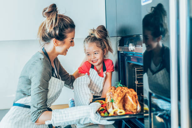 Mother and daughter preparing turkey Happy mother and cute little daughter taking roasted turkey out of the oven family dinners and cooking stock pictures, royalty-free photos & images