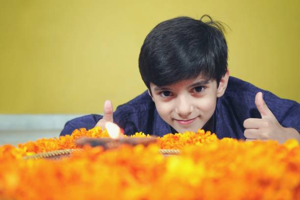 one happy smiling indian asian boy looking with a aarti pooja or prayer thaali with a flame, jyot, diya, deepak flame and marigold flowers gives thumbs up - facial expression child asia asian and indian ethnicities imagens e fotografias de stock