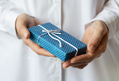 Woman in white doctor robe holding gift box in decorated craft paper in hands. Selective focus. Christmas and New Year concept.