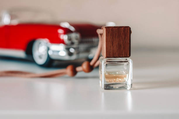 botella pequeña de vidrio con líquido aromático. ambientador de aire de coche cerca del modelo de coche de juguete. - car freshner fotografías e imágenes de stock